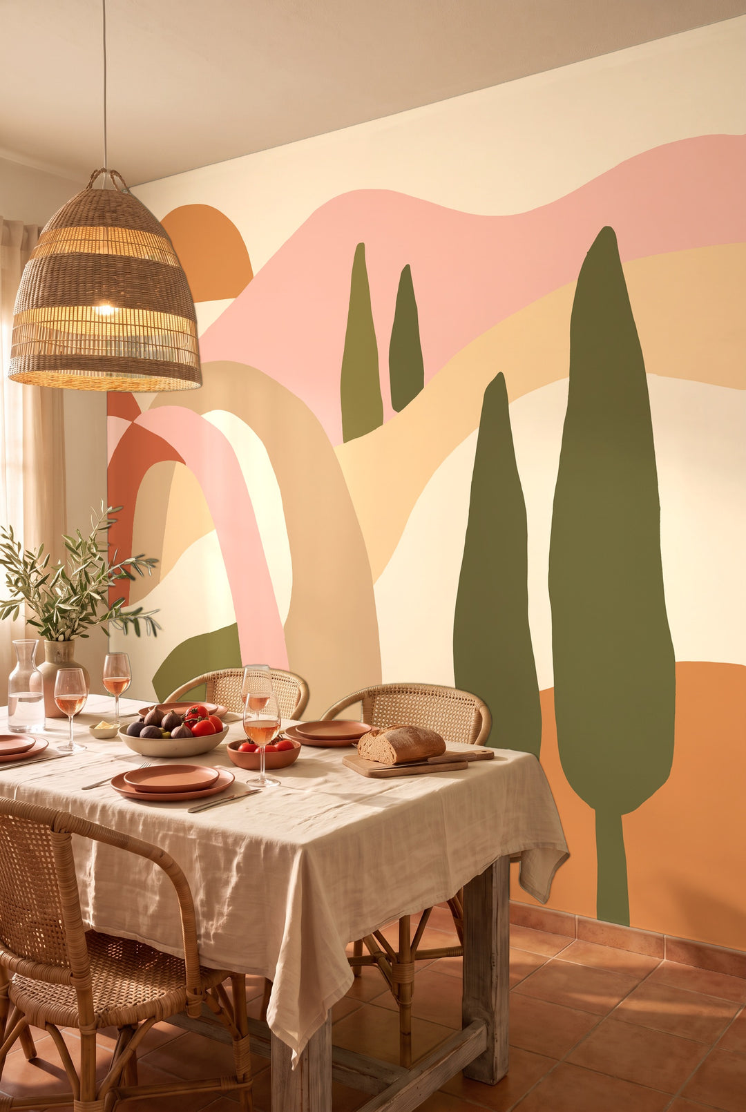 Salle à manger méditerranéenne avec table dressée et chaises en rotin devant un papier peint panoramique de collines toscanes terracotta et rose