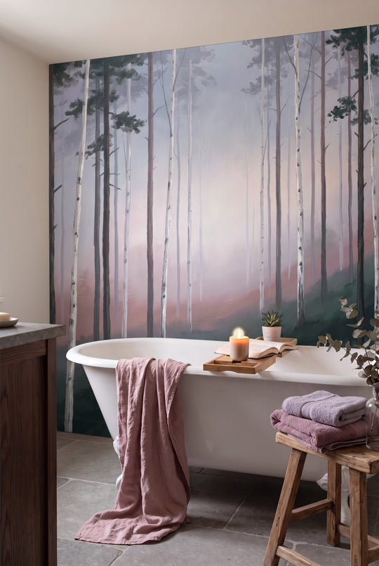 Salle de bain avec baignoire blanche, bougie et serviettes roses devant un papier peint panoramique de forêt de bouleaux dans une brume rose et mauve