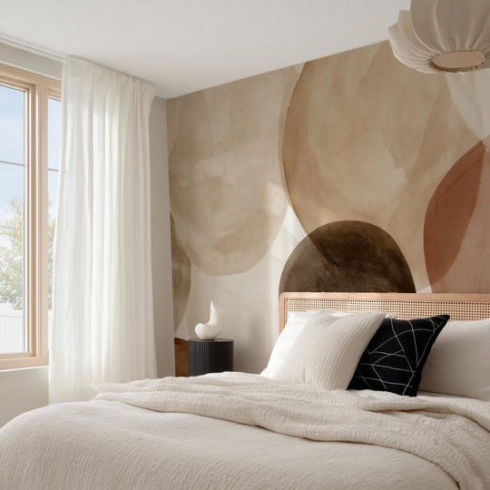 Chambre lumineuse avec tête de lit cannée et voilages devant un papier peint panoramique de galets aquarelle