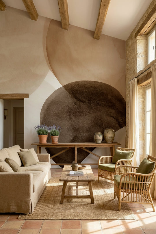 Salon sous poutres apparentes avec fauteuils en rotin devant un papier peint panoramique abstrait beige et brun