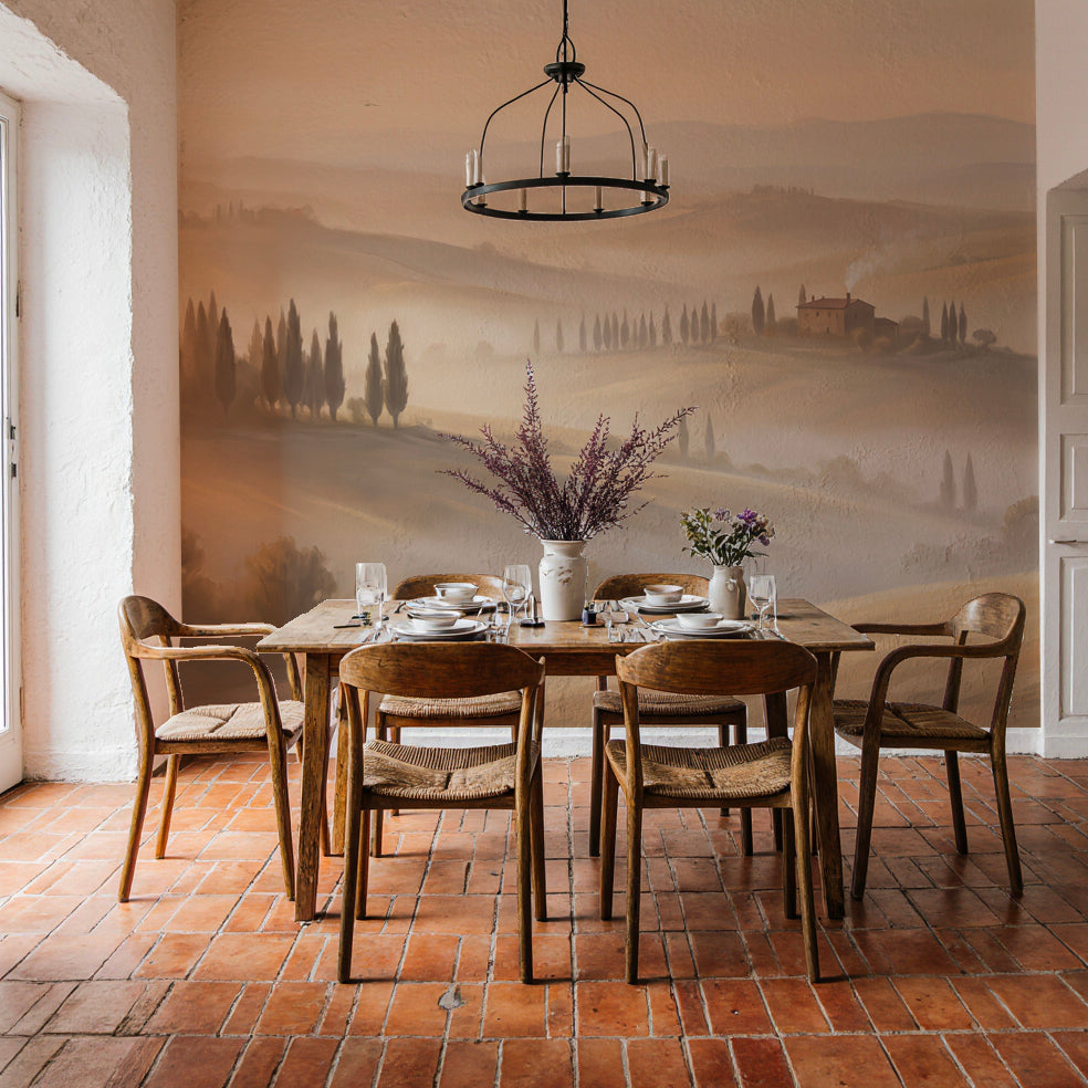 Salle à manger aux tomettes et table en bois devant un papier peint panoramique de collines toscanes