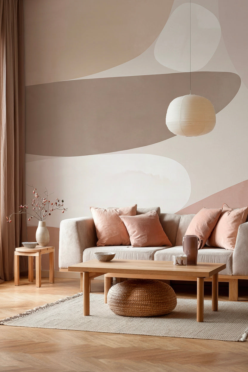 Salon avec canapé crème, coussins rose poudré et suspension en papier devant un papier peint panoramique abstrait de formes organiques beige et rose