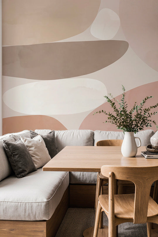 Coin repas avec banquette et table en bois devant un papier peint panoramique abstrait beige, taupe et rose