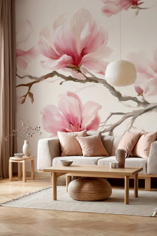 Salon avec canapé crème et coussins rose poudré devant un papier peint panoramique de branches de magnolias roses sur fond crème