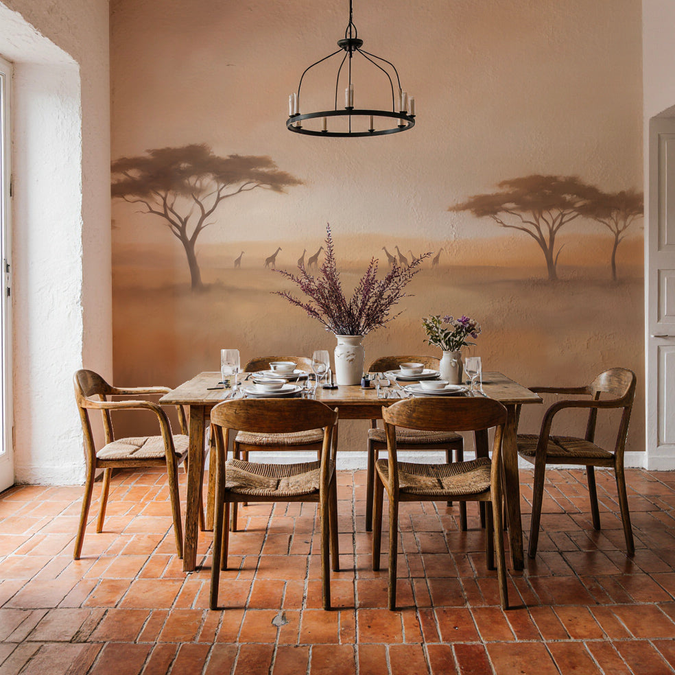 Salle à manger aux tomettes et table en bois devant un papier peint panoramique de savane et girafes